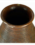 Close-up of a brown ribbed Indonesian pottery vase with a chipped rim and wide dark opening, Lombka Island.