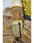 Close-up of gold jeweled cuff and articulated fingers on Indonesian puppet wearing patterned golden fabric clothing.
