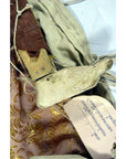 Brown wooden Indonesian puppet with white L-shaped end on patterned fabric, handwritten tag beside it.