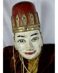 Close-up of Indonesian puppet with tangled strings, red and gold hat, and red lips on a white background.