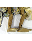 Brown wooden Indonesian puppet with jointed legs, patterned fabric clothing, lying on a white surface.