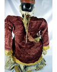 Red velvet Indonesian puppet with yellow trim and matching hat, viewed from the back.