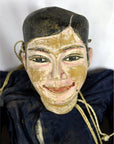 Close-up of Indonesian puppet with blue clothing, black hair, smiling face, and tangled strings on white background.