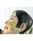 Close-up of Indonesian puppet head with black hair, tangled strings, and a smiling face on a white background.