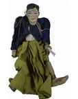 Close-up of Indonesian puppet with painted face, dark jacket, green skirt, tangled strings on white background.