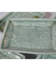 Light green celadon ceramic serving bowls with floral pattern, stacked and overlapping on a white surface.