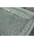 Close-up of a pale green rectangular Japanese celadon serving bowl with floral pattern.