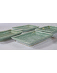 Close-up of five green Japanese Celadon ceramic serving bowls overlapping on a white surface.