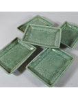 Green celadon ceramic Japanese serving bowls with floral patterns arranged on a white surface.