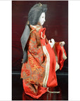 Close-up side view of Japanese doll with long black hair, white face, red kimono with gold patterns.