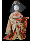 Close-up of an antique Japanese doll in a floral kimono and flower headdress against a black background.