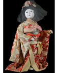 Close-up of an antique Japanese doll in a floral kimono and flower headdress against a black background.