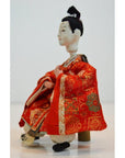 Red and gold kimono Japanese doll with styled black hair, seated, Kyoto-made, close-up.