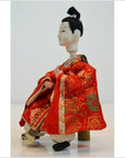 Red and gold kimono Japanese doll with styled black hair, seated, Kyoto-made, close-up.