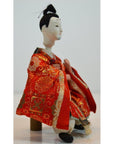 Red patterned fabric Japanese doll on wooden stool, plain background, Kyoto-made, close-up product view.