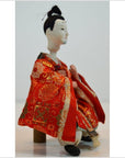 Red patterned fabric Japanese doll on wooden stool, plain background, Kyoto-made, close-up product view.