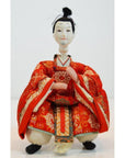 Close-up of a Kyoto-made Japanese doll in an ornate red kimono, seated with hands placed gracefully in front.