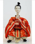 Close-up of a Kyoto-made Japanese doll in an ornate red kimono, seated with hands placed gracefully in front.