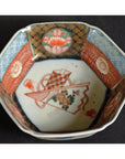 Red, blue, and gold porcelain Imari octagonal bowl with floral and geometric designs on white background, close-up.