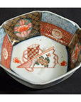 Close-up of a white porcelain Japanese Imari bowl with red, blue, and gold floral and geometric patterns.