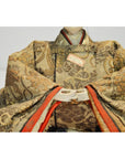 Close-up of Japanese Taisho Samurai Doll in ornate gold and brown patterned kimono with folded hands.