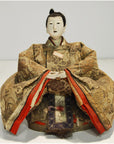 Ornate kimono Japanese Taisho Samurai Doll, folded arms, seated on plain surface, white background, close-up.
