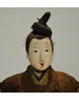 Close-up of Japanese Taisho samurai doll with painted face, topknot hairstyle, and brown kimono.