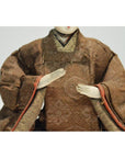 Close-up of a Japanese Taisho samurai doll wearing a brown kimono, hands positioned in front.