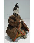 Close-up of Japanese Taisho Samurai Doll in ornate brown and red robes, seated with hands together.