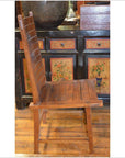 Brown teak wood side chair with high slatted back on wooden floor, positioned in front of a painted cabinet.