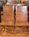 Brown teak wood side chairs with wooden seats and backs, side by side on wooden floor in vintage room setting.