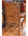 Brown teak wood side chair with slatted backrest on polished floor, furniture and red vase in background.