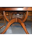 Brown wood Javanese oval dining table with leaf, viewed from below, surrounded by wooden chairs on a grey floor.
