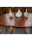 Brown wood Javanese oval dining table with leaf, three ceramic vases, animal pottery centerpiece, wooden chairs around.
