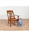 Brown wooden lounge chair with slanted back on wooden floor next to blue floral ceramic vase indoors.