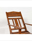 Brown wooden lounge chair with slanted back near a white brick wall, indoors.