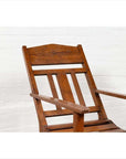 Brown wooden lounge chair with slanted back near a white brick wall, indoors.