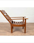Brown wooden lounge chair with slanted back on wooden floor next to white brick wall indoors.