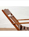 Brown wooden lounge chair with slanted back, placed indoors against a white brick wall and wooden floor.