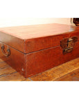 Black lacquer leather trunk with butterfly hardware and metal handles on a wooden floor.
