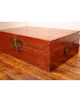 Black lacquer leather trunk with butterfly hardware and metal handles on a polished wooden floor.