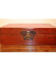 Black lacquer leather trunk with butterfly hardware on a wooden floor against a light-colored wall.
