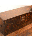 Black lacquer trunk with metal latch and painted designs on a wooden floor.