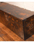 Black lacquer trunk with metal handles and painted designs on a wooden floor.