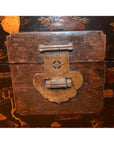 Close-up of an ornate aged brass latch on a black lacquer trunk with gold decorative patterns.
