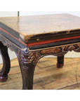 Black lacquered wood side table with ornate carved legs and a worn rectangular top on a wooden floor.