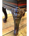 Close-up of black lacquered wood side table leg with carved guardian design on a wooden floor.