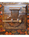 Close-up of decorative metal latch and sliding lock on black lacquered trunk with floral and landscape designs on stand.