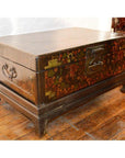 Black lacquered wood trunk with painted floral designs, metal handles, and latch on wooden floor.