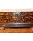 Black lacquered wood trunk with floral designs, metal latch, and raised legs on a wooden floor.